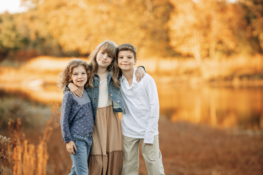 Three siblings hugging with a golden background of a lake and fall colors
